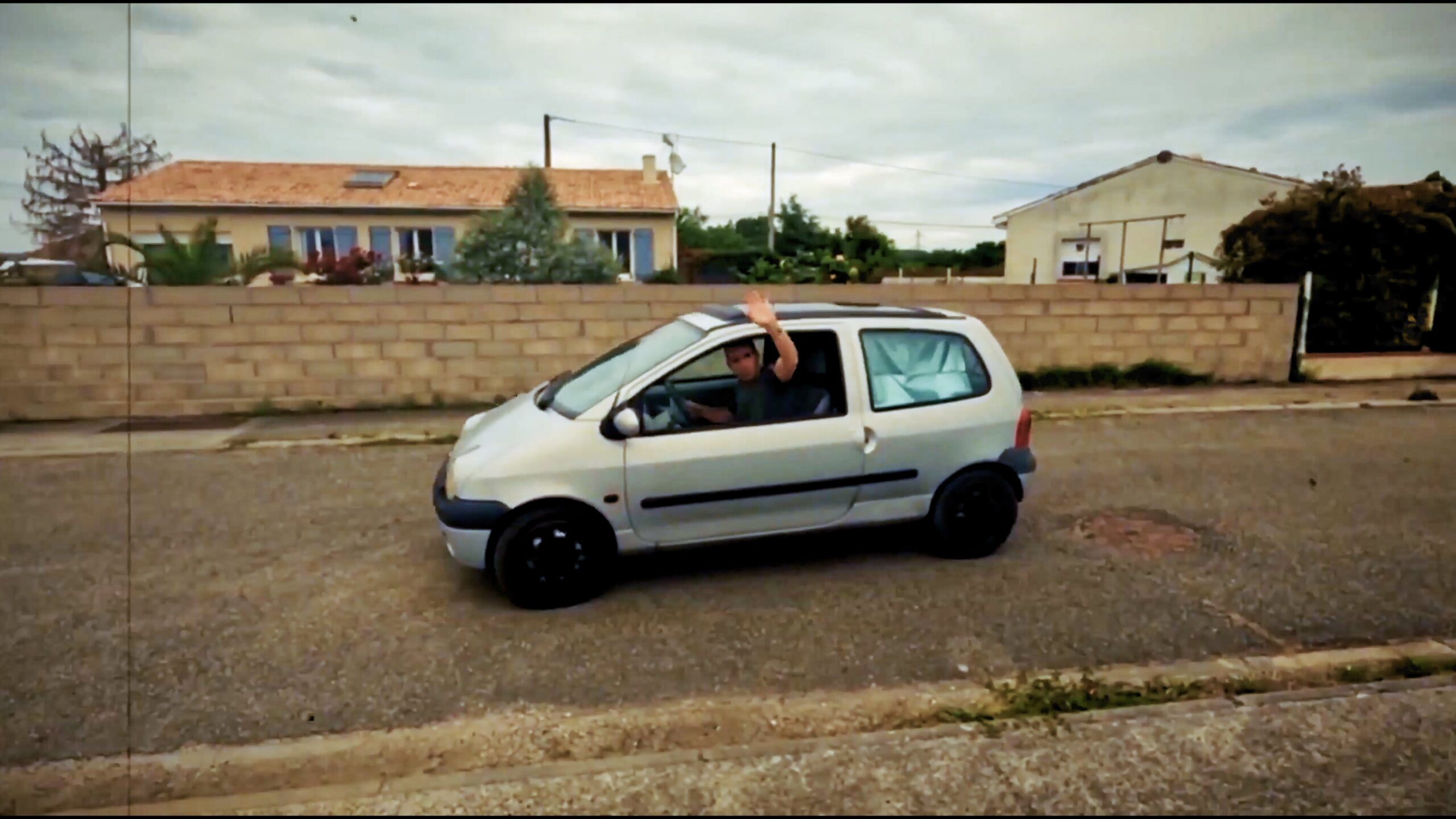 Une petite Twingo blanche sur la route, avec le conducteur qui salue
